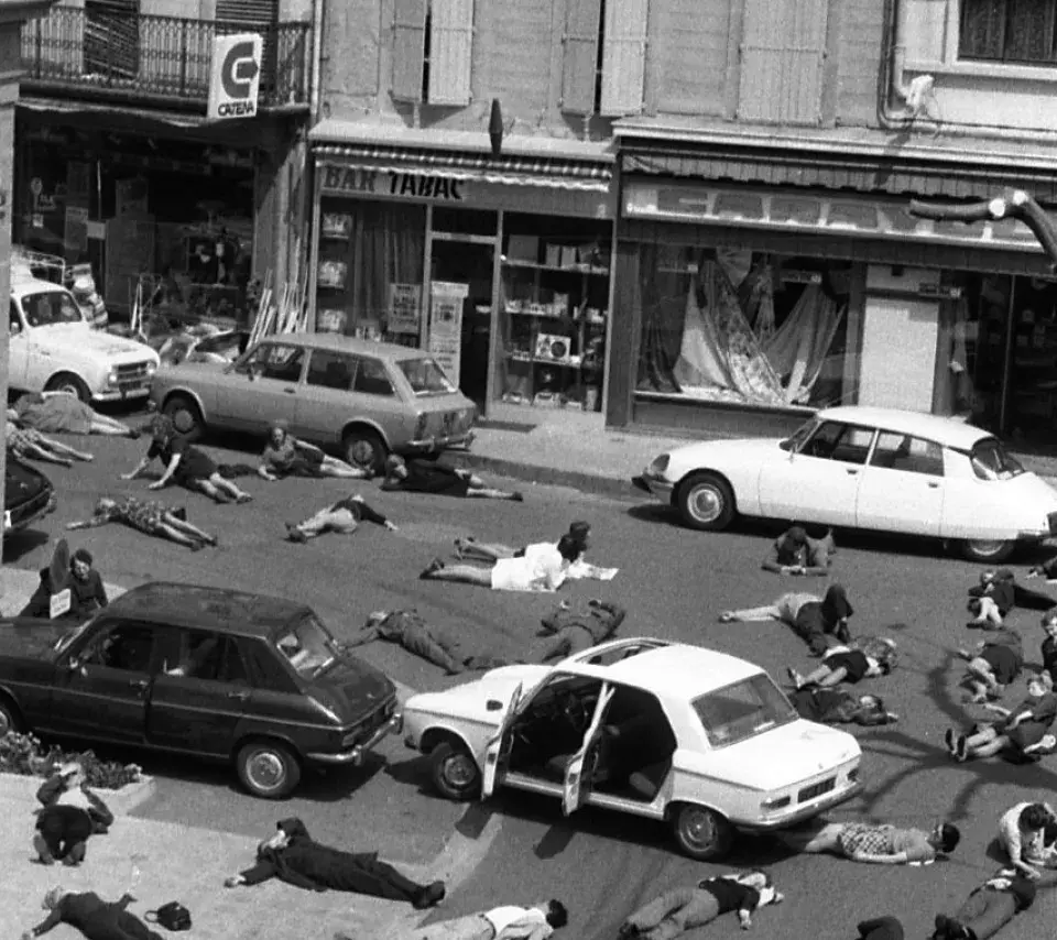 Photo : Vue d'ensemble en plongée d'un grand nombre de personnes couchées au milieu de la rue et sur les trottoirs (comme si elles étaient mortes), voitures arrêtées portières ouvertes, 1973. Cliché pris lors de l'opération médiatique "Mazamet ville morte" organisée par la Sécurité routière.